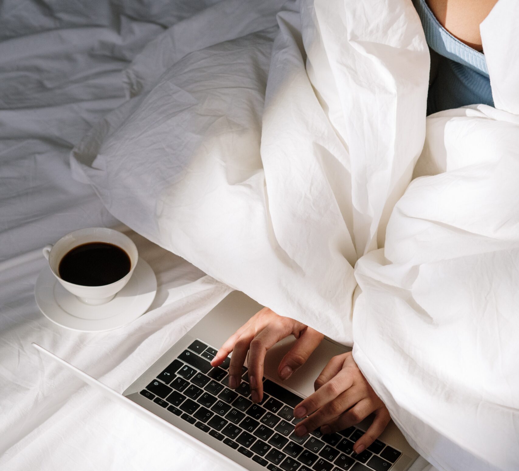 woman working from bed on laptop with coffee doing remote work