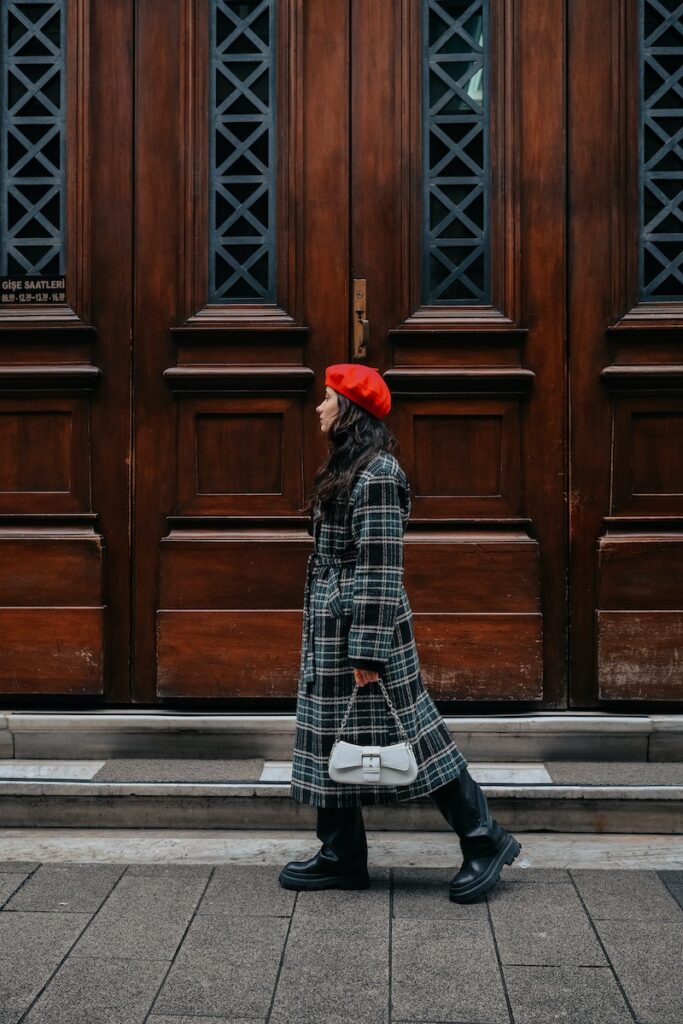 Young Brunette Wearing a Checkered Coat and Red Beret and Walking on a Sidewalk