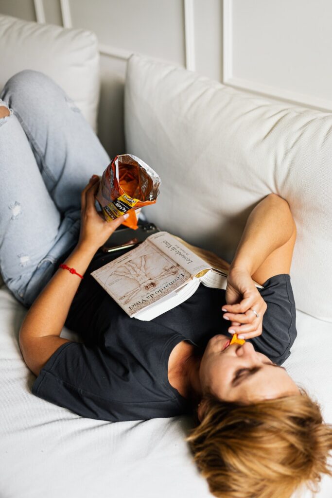 Woman Lying on Bed Eating Chips
