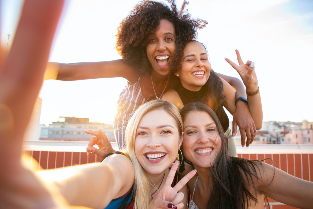 Cheerful young diverse women showing V sign while taking selfie on rooftop. How to Manifest Something
