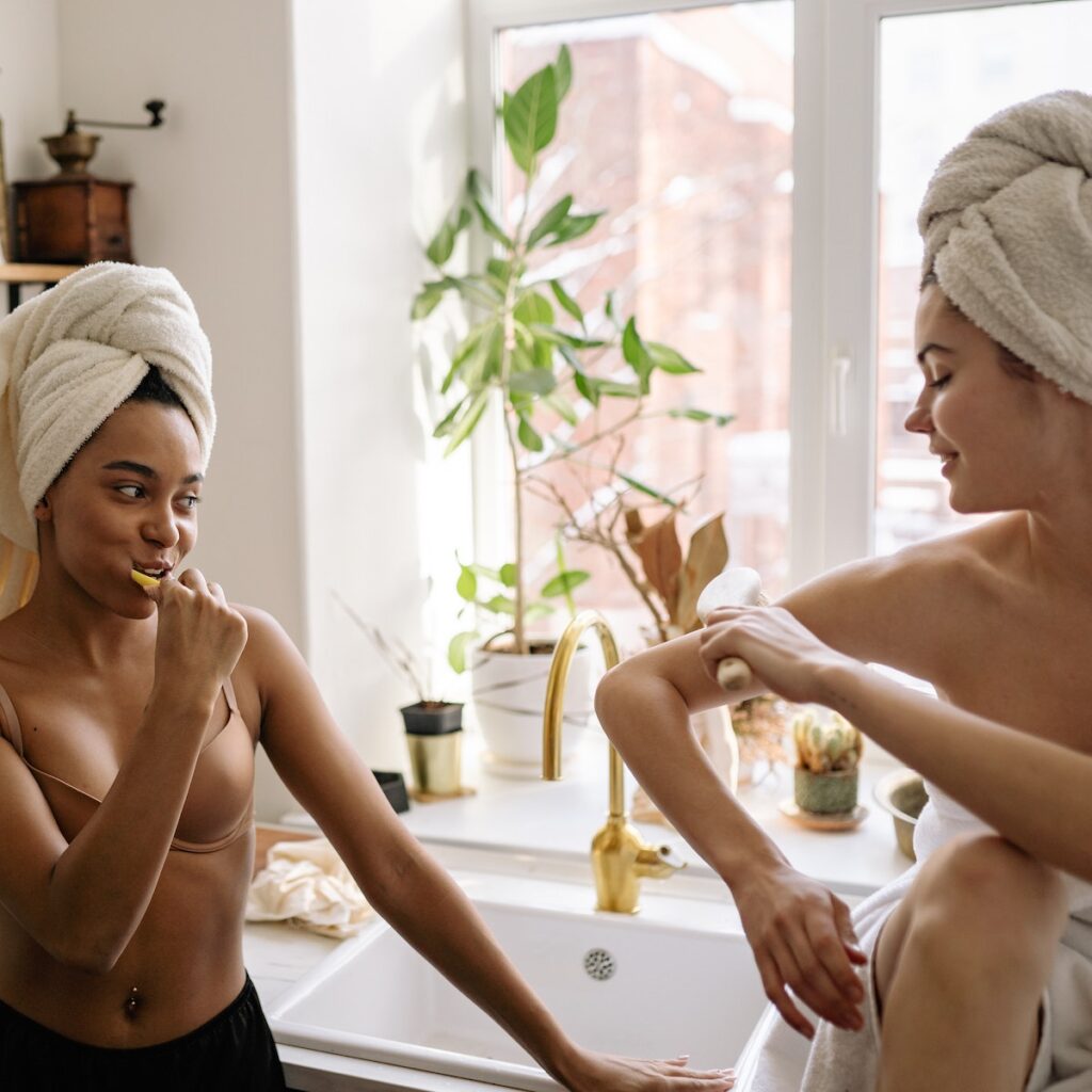 Women in Head Towels Near a Sink With Faucet brushing teeth with natural dental care product