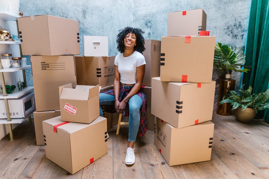 Photograph of a Woman in a White Shirt Sitting Beside Cardboard Boxes who used money in her emergency fund to relocate