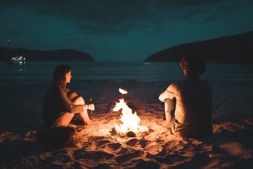 man and woman with bone fire sitting on seashore romantic relationship
