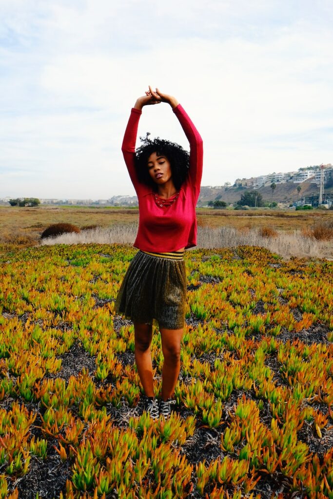 a woman standing in a field with her arms above her head