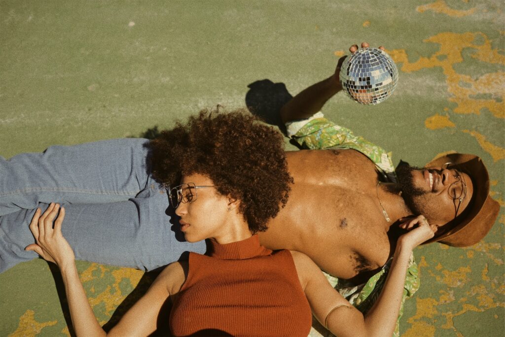 woman in brown turtleneck sleeveless top lying on man's stomach wearing green button-up collared shirt holding disco ball in a romantic relationship
