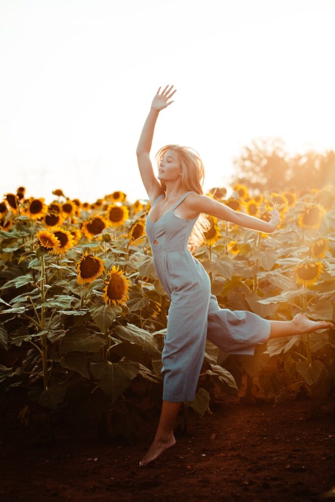 close up photography of woman who has confidence dancing beside sunflower field during golden hour